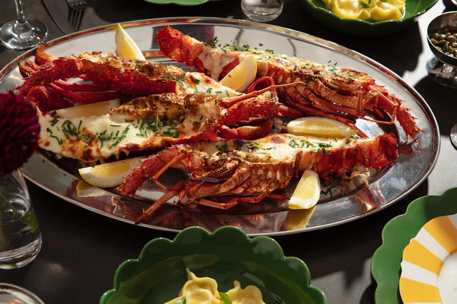 A silver platter of split grilled lobster tails with lemon, on a set dining table