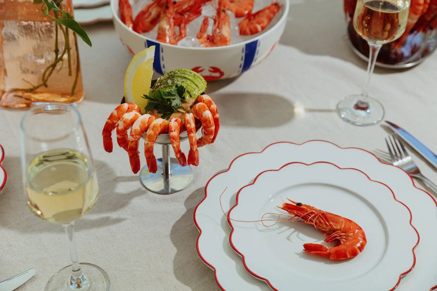 A prawn cocktail in a footed bowl and a single prawn on a red-rimmed plate, on a set restaurant table